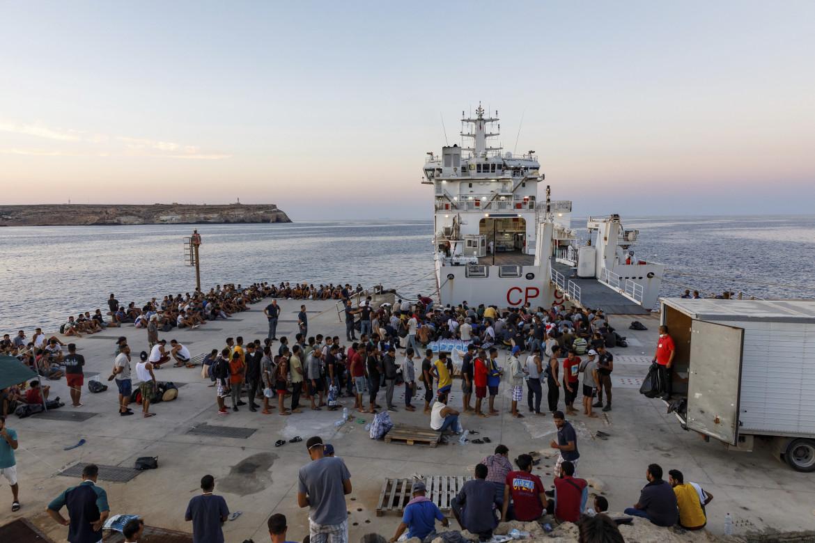 Migranti al porto di Lampedusa in procinto di imbarcarsi su una nave della Guardia Costiera, foto Ap