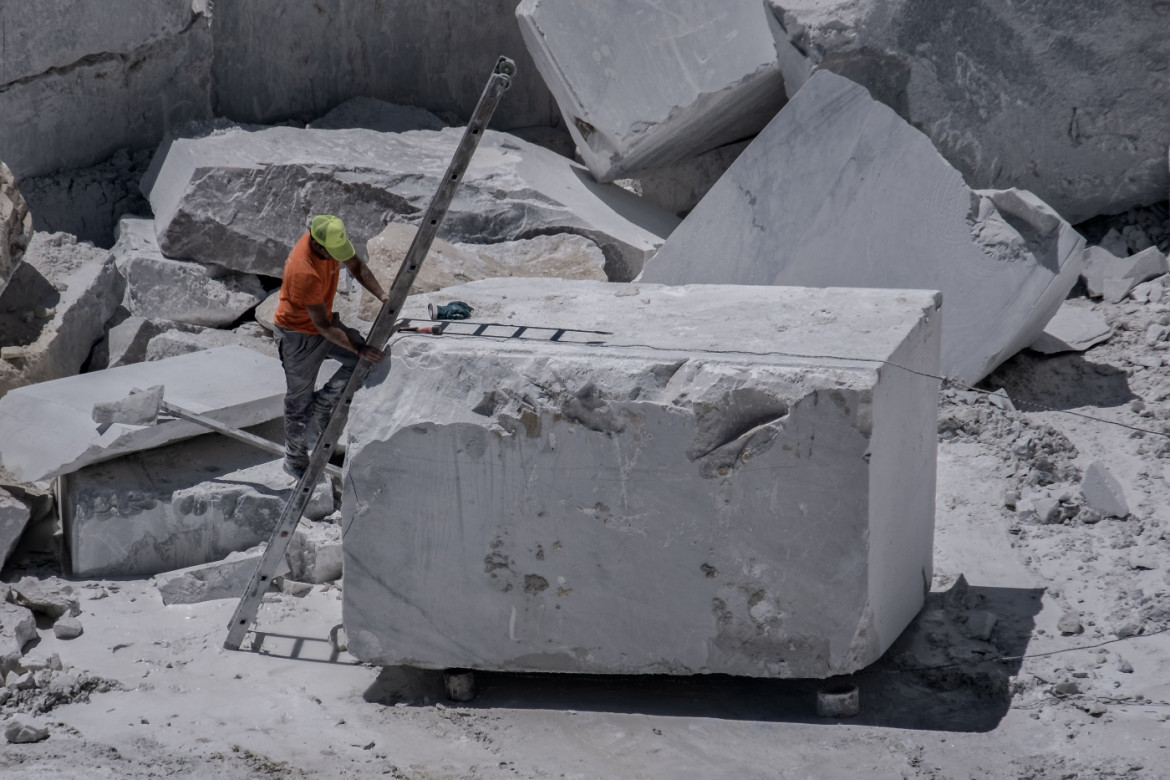 03-operaio-del-settore-lapideo-supervisiona-le-lavorazioni-di-riquadratura-meccanica-con-filo-diamantato-di-un-grande-blocco-di-marmo-bianco-appena-estratto-su