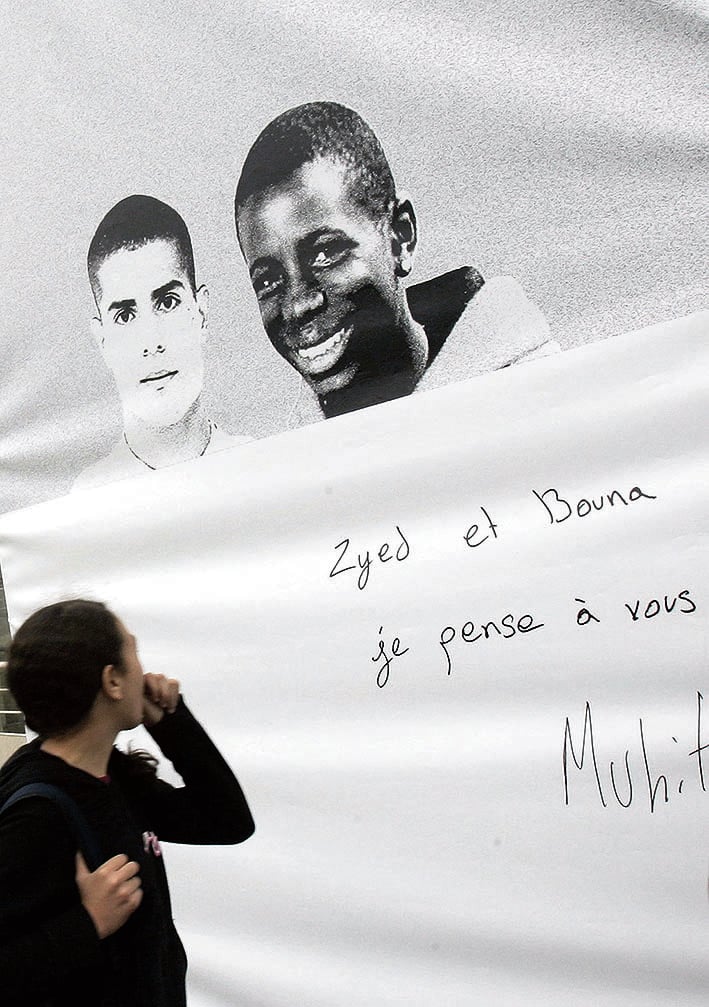 Clichy-sous-Bois resident walks Friday, Oct. 20, 2006 past photos of Zyed Benna, rear left, and Bouna Traore, who died after being electrocuted in a power substation on Oct. 27, 2005 in Clichy-Sous-Bois, outside Paris .In the minds of young people, it was fear of police that drove Zyed and Bouna to their deaths and started of three weeks of rioting, car burnings and attacks on police that raged through housing projects and laid bare decades of discrimination against France's black and Arab citizens. The picture reads 