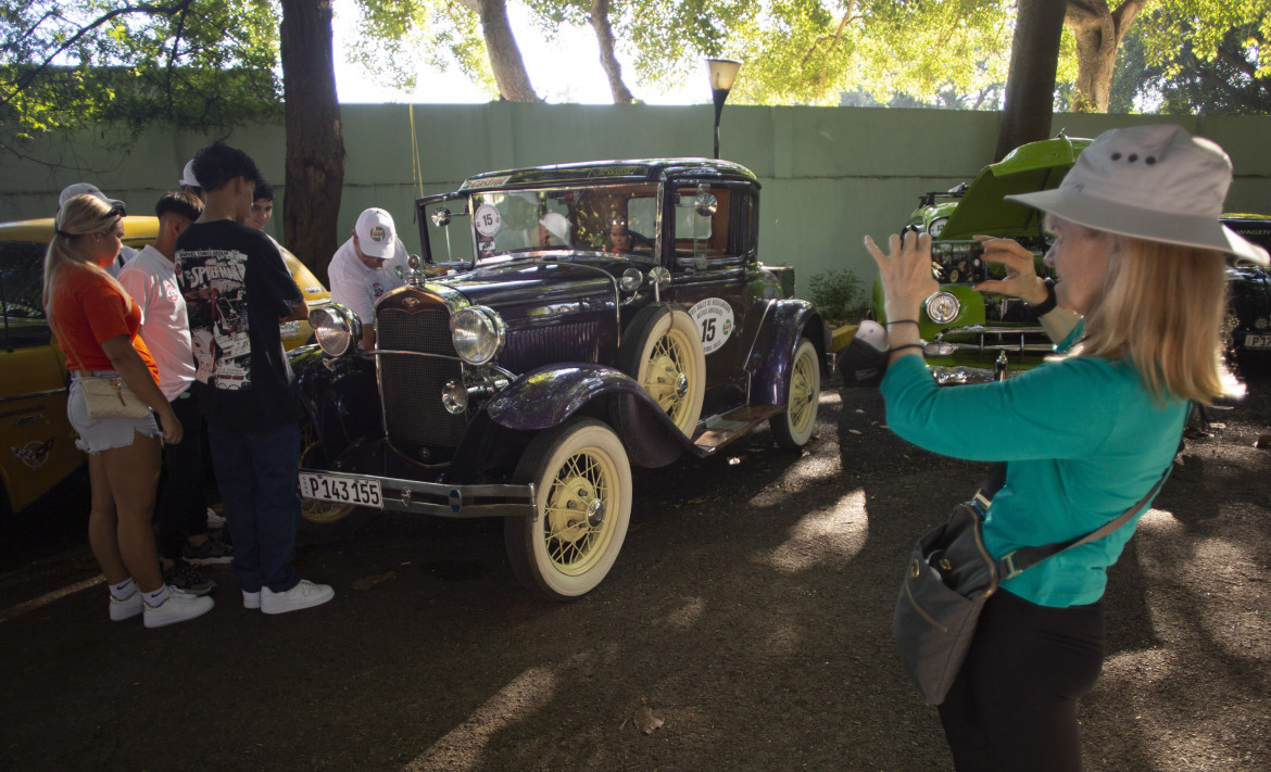 Una turista scatta una foto a L'Avana al rallly di auto storiche il 3 dicembre 2023, foto Ismael Francisco /Ap