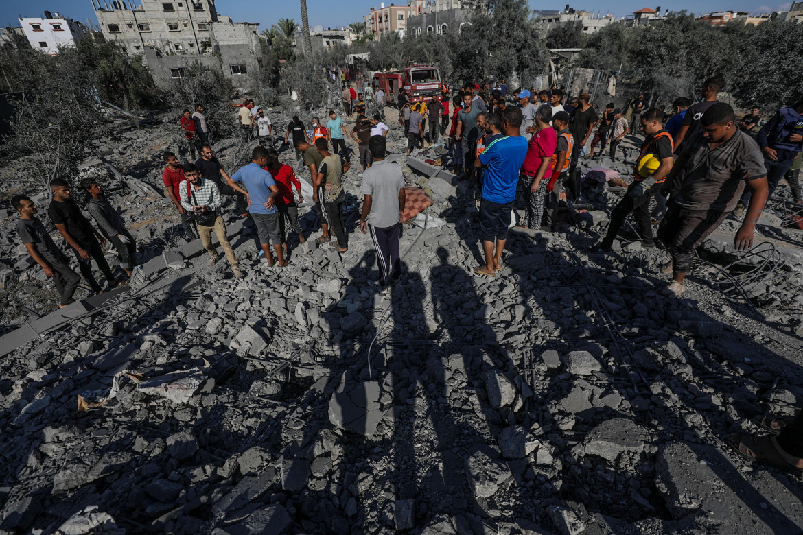 Palestinesi cercano tra le macerie di una casa distrutta in seguito agli attacchi aerei israeliani nel campo profughi di Al-Maghazi