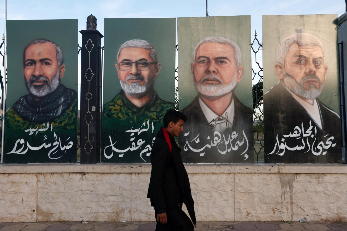 Una persona passa davanti a dipinti raffiguranti (da destra a sinistra) il leader di Hamas Yahya Sinwar, il defunto leader di Hamas Ismail Haniyeh e i defunti comandanti militari di Hezbollah Ibrahim Aqil e Saleh Sorour foto di Yahya Arhab/Ansa