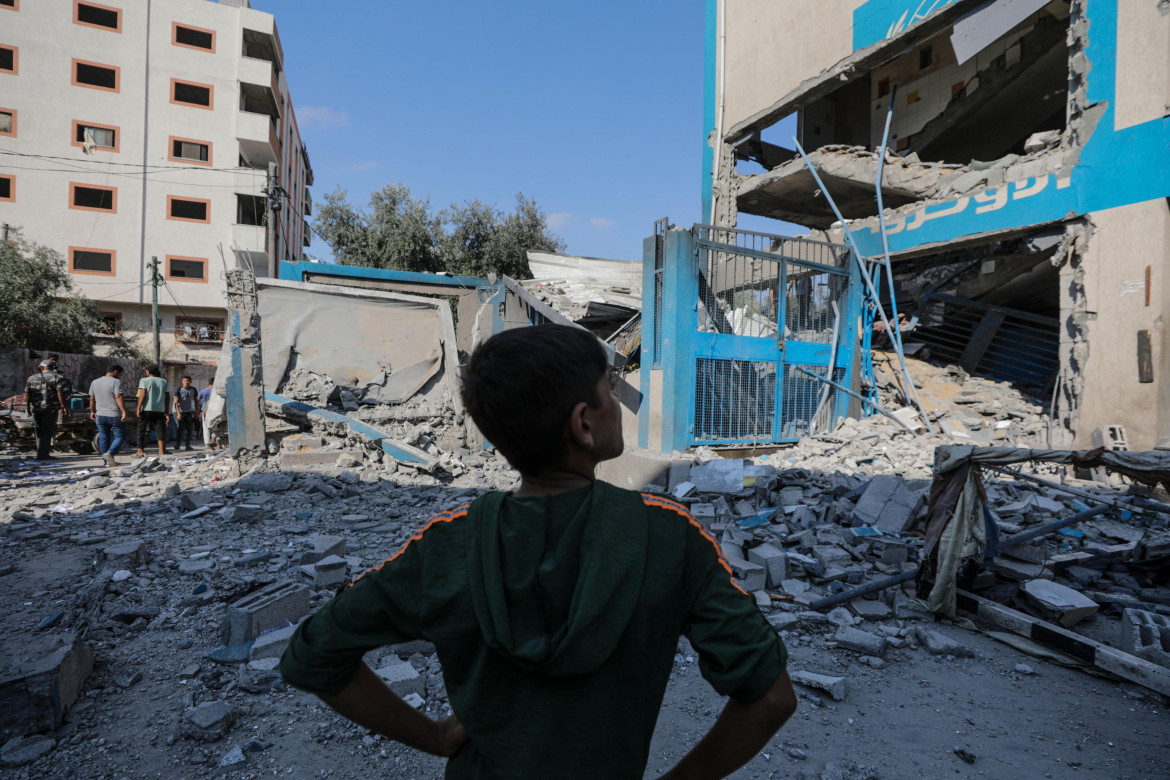 Un ragazzo palestinese in piedi vicino alle macerie di una scuola Unrwa dopo un attacco aereo israeliano nel campo profughi di Al Nuseirat, nella Striscia di Gaza foto di Mohammed Saber/Ansa