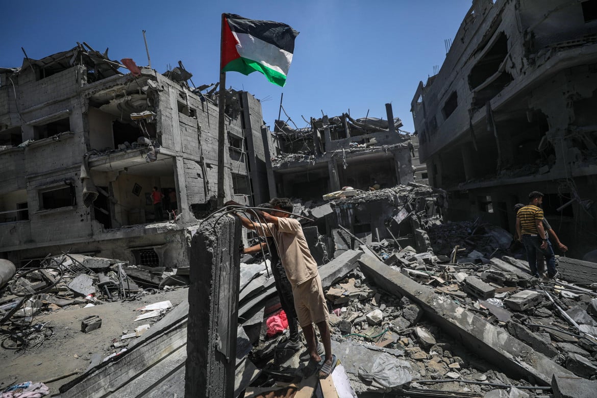 Palestinesi issano una bandiera palestinese accanto alla loro casa distrutta in seguito a un attacco aereo israeliano nel campo profughi di al-Bureij, nel sud della Striscia di Gaza (Mohammed Saber, Ansa)